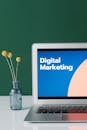 A laptop displaying 'Digital Marketing' with a minimalist floral decor in a glass vase.